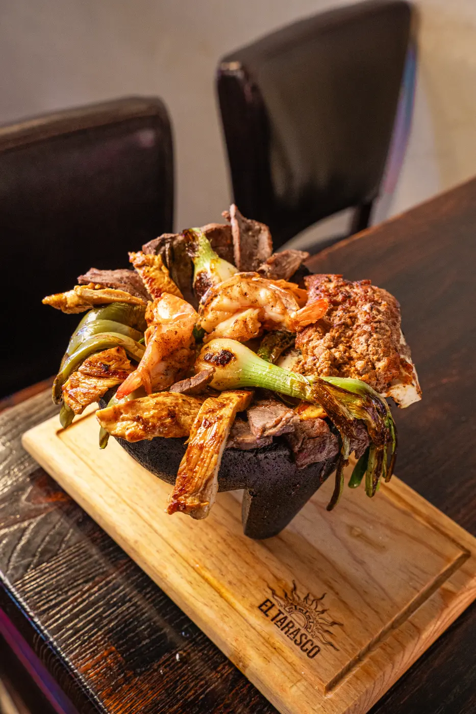 A molcajete of grilled shrimp, chicken, steak, cactus and spring onions on a branded El Tarasco board