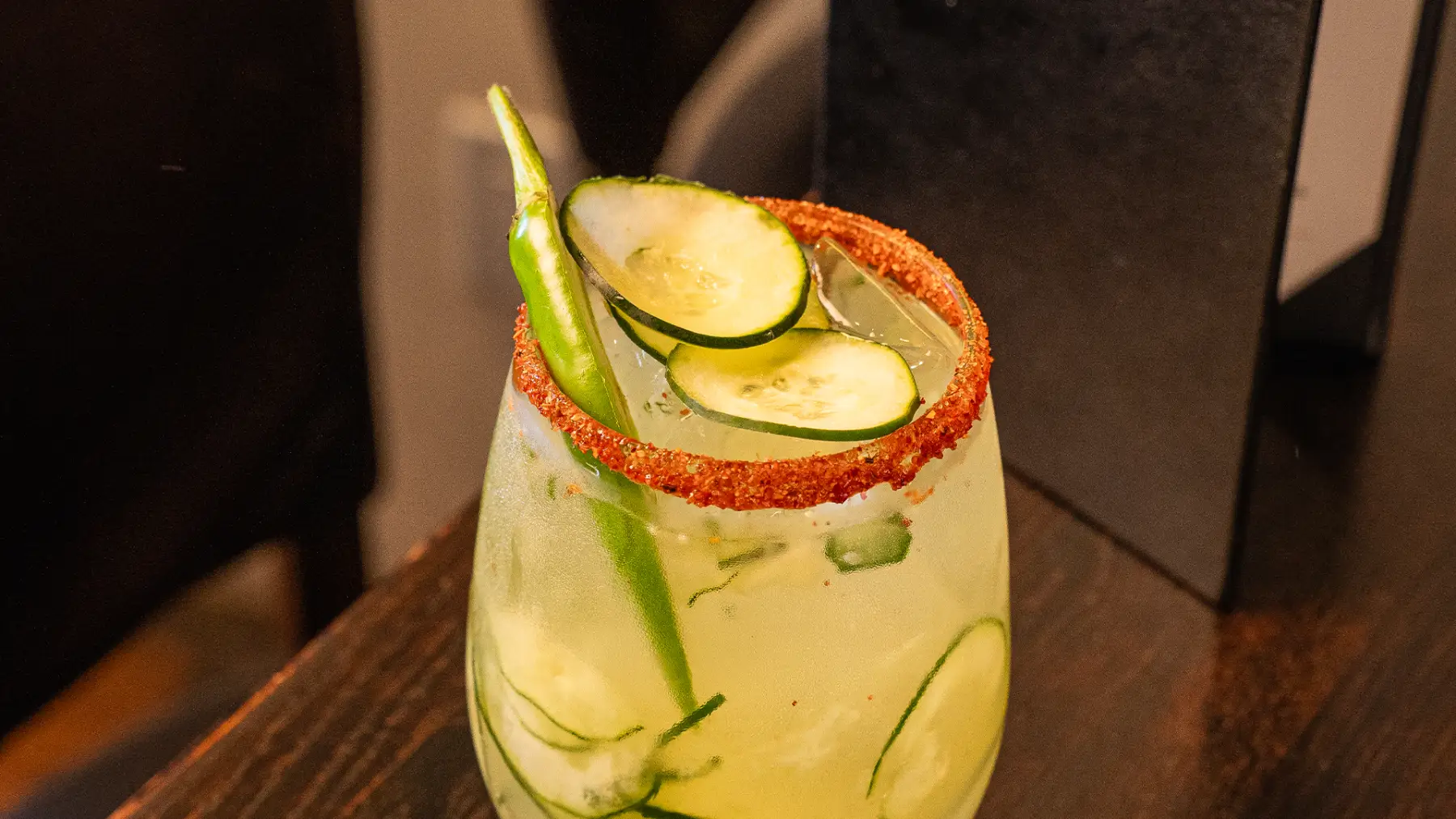 A cucumber margarita with a chile-salted rim, garnished with cucumber and a serrano pepper