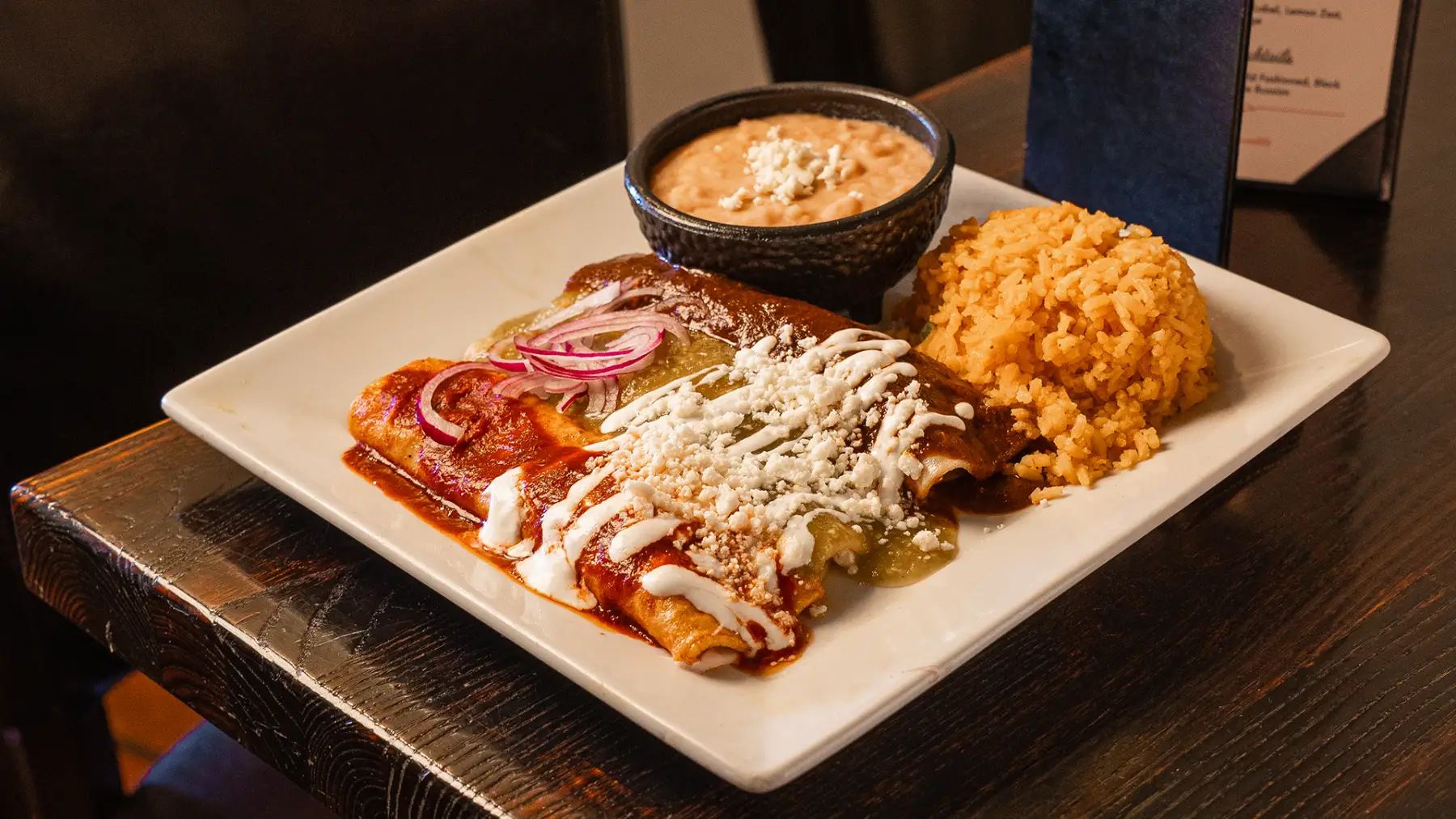 An enchiladas plate with red and green sauce, crema, cotija, Mexican rice and beans